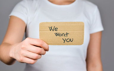 Young women hand  holding cardboard paper with We want you  phrase hand written.