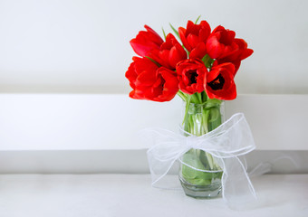 red tulips bouquet in a glass with white tie and background