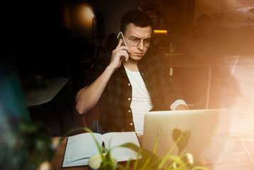 Mature handsome smart male freelancer dressed in stylish denim clothing sets up a modern digital device and checks the schedule on a smartwatch while sitting at a wooden table with a laptop.