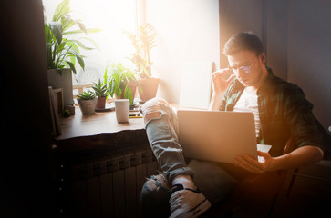 Mature handsome smart male freelancer dressed in stylish denim clothing sets up a modern digital device and checks the schedule on a smartwatch while sitting at a wooden table with a laptop.