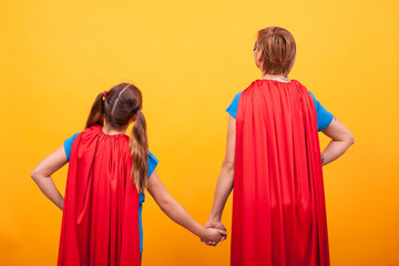 Fototapeta premium Back view of mother and her little girl dressed like superheros holding hands.