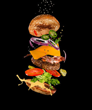 Tasty hamburger with flying ingredients on dark background. High resolution image.