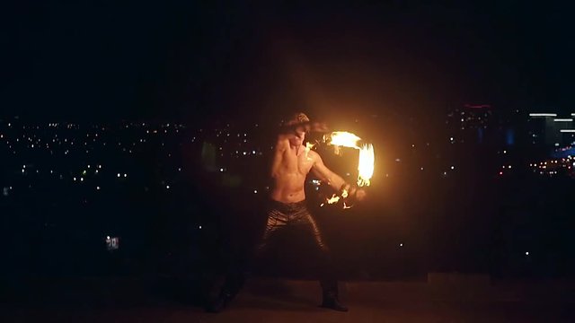 Young blond male spins two burning pois. Slow motion.