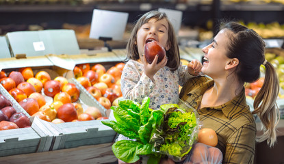 Family in the supermarket. Beautiful young mom and her little daughter smiling and buying food.