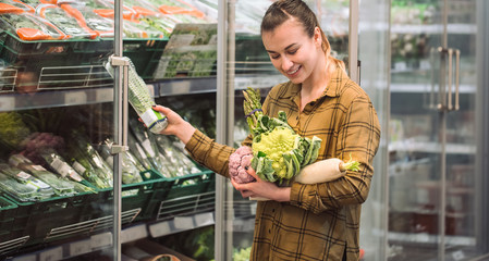 Woman in the supermarket. Beautiful young woman holds in hands fresh organic vegetables and opens the fridge in the supermarket