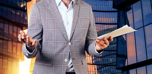 A man holding documents and a ballpoint pen spreading his hands against the background of a skyscraper. The concept of business success.