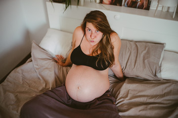 Pregnant woman sitting on bed making fatty face