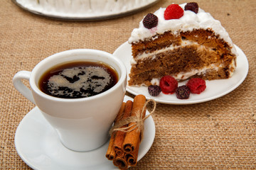 Cup of coffee, cinnamon and slice of biscuit cake decorated with whipped cream and raspberries.
