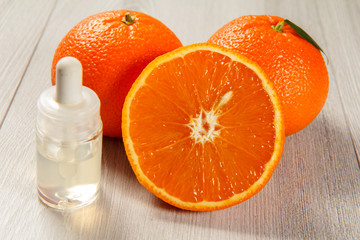 Cut orange with two whole oranges and bottle with aromatherapy oil on wooden boards.