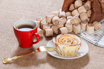 Board game lotto on sackcloth. Wooden lotto barrels in bag and game cards with cup of coffee and homemade cookie on plate.