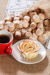 Board game lotto on sackcloth. Wooden lotto barrels in bag and game cards with cup of coffee and homemade cookie on plate.