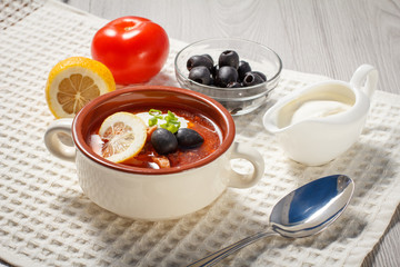 Soup saltwort with meat, potatoes, tomatoes, lemon, black olives and sour cream in ceramic soup bowl.