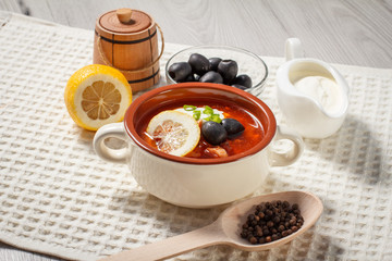 Soup saltwort with meat, potatoes, tomatoes, lemon, black olives and sour cream in ceramic soup bowl