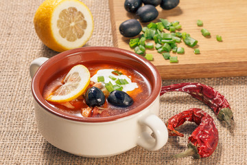 Soup saltwort with meat, potatoes, tomatoes, lemon, black olives and sour cream in ceramic soup bowl