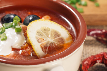 Soup saltwort with meat, potatoes, tomatoes, lemon, black olives and sour cream in ceramic soup bowl
