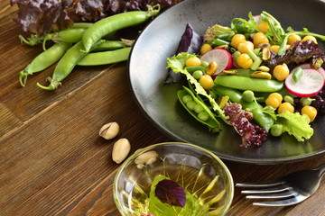 Healthy vegetarian bowl salad with chickpeas, green peas, radish and pistachios, copy space