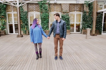 Woman with purple hair holding a hand of a man in a plaid shirt. A couple in an embrace in the street.