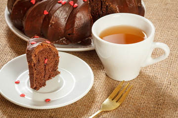 Homemade chocolate cake decorated with small caramel hearts and cup of tea.
