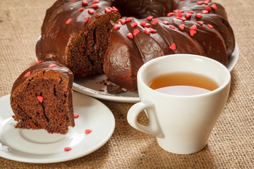 Homemade chocolate cake decorated with small caramel hearts and cup of tea.