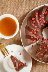 Homemade chocolate cake decorated with small caramel hearts and cup of tea.