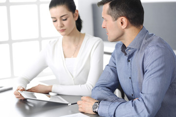 Cheerful smiling businessman and woman working with tablet computer in modern office. Headshot at meeting or workplace. Teamwork, partnership and business concept 