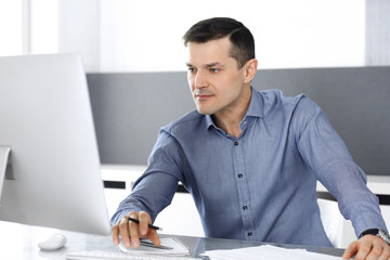Fototapeta premium Businessman working with computer in modern office. Headshot of male entrepreneur or company director at workplace. Business concept