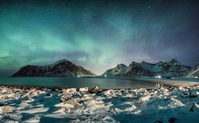 Aurora borealis with stars over mountain range with snowy coastline at Skagsanden beach