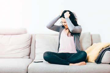 Obraz premium beautiful woman sitting on couch angry and frustrated shouting and tearing off hair while looking at the mobile phone - stress, communication problems and anger concept