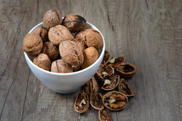 Pile of whole  and cracked walnuts  in a white ceramic bowl on a table.