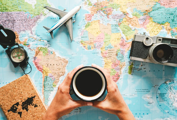 Top view of young woman planning her vacation using world map while drinking coffee - Tourist...