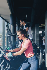Fototapeta na wymiar Young fit man and woman running on treadmill in modern fitness gym.