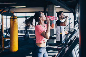 Young fit man and woman running on treadmill in modern fitness gym.