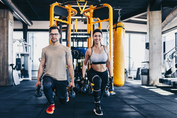 Young fit and attractive man and woman exercising workout with kettlebell in modern fitness gym.