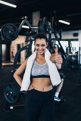 Young attractive woman after successful workout posing and smiling in modern fitness gym while showing thumb up