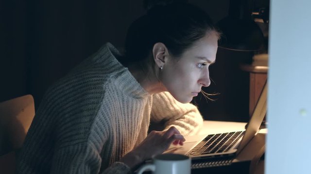 Concentrated and tired Young Woman working on laptop at night. Medium shoot. 4k. 