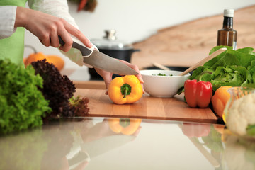 Unknown human hands cooking in kitchen. Woman slicing yellow bell pepper. Healthy meal, and vegetarian food concept