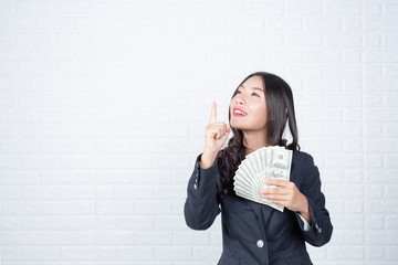 A young businesswoman holds a dollar note on a white brick wall background.