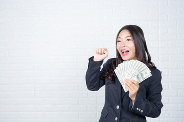 A young businesswoman holds a dollar note on a white brick wall background.