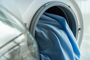 Open door in washing machine with blue bed sheets inside close up