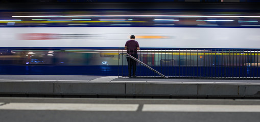 People in a trainstation with motion blurred trains moving fast (color toned image)