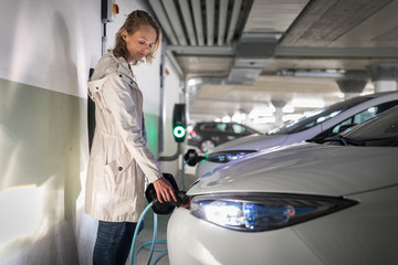 Young woman charging an electric vehicle in an underground garage equiped with e-car charger. Car...