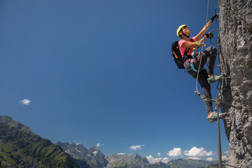 Pretty, female climber on a via ferrata - climbing on a rock in Swiss Alps