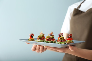Chef holding plate with tasty canapes on light background