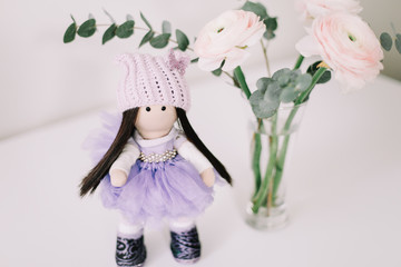 Cute doll  and a bouquet of spring flowers on white background. Handmade doll in a dress. 