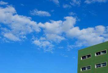 Minimalistic urban background. Green house against the blue sky with clouds