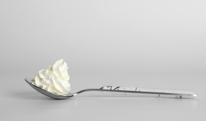 Spoon with whipped white cream on light background