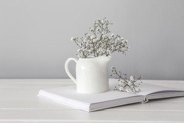 Open book with jug and flowers on white wooden table