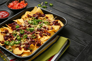 Baking dish with tasty nachos, minced meat and chili on wooden table