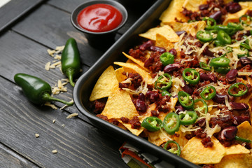 Baking dish with tasty nachos, minced meat and chili on wooden table
