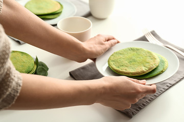 Woman putting plate with freshly fried green pancakes on table